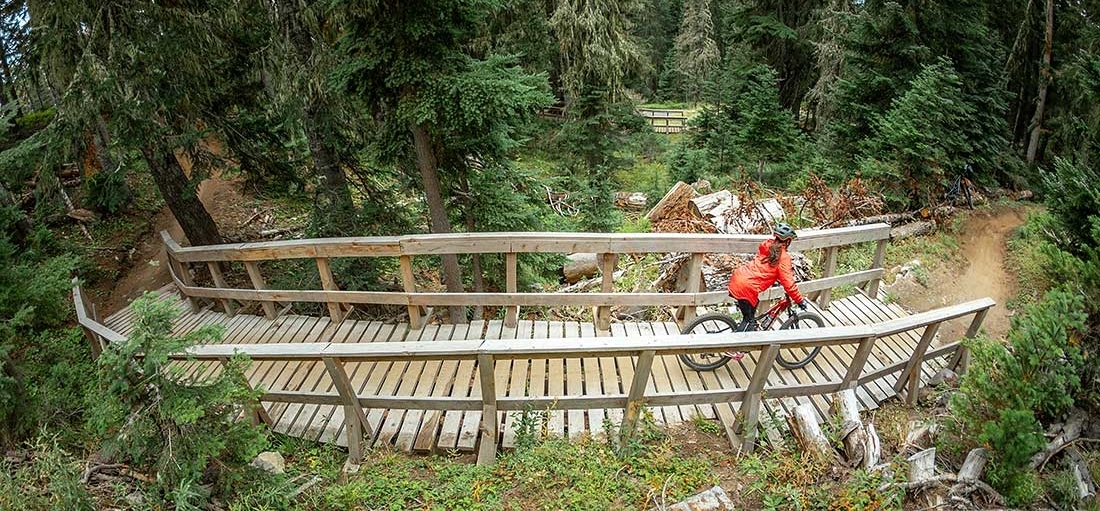 FEMAILE MOUNTAIN BIKER IN RED JACKET CROSSING A BRIDE IN THE TIMBERLINE BIKE PARK