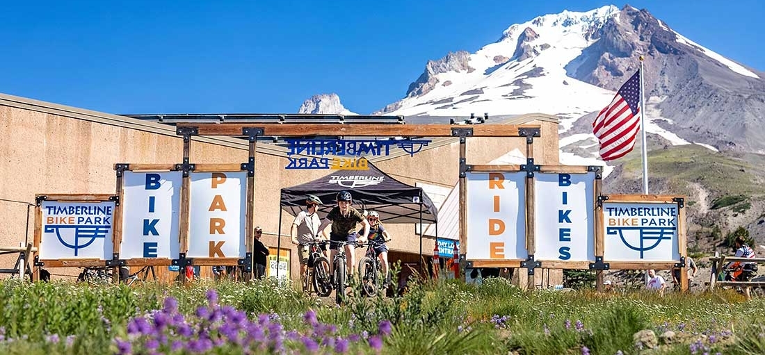 YOUTH MOUNTAIN BIKERS ENTERING THE TIMBERLINE BIKE PARK ENTRANCE WITH MT HOOD IN THE BACKGROUND