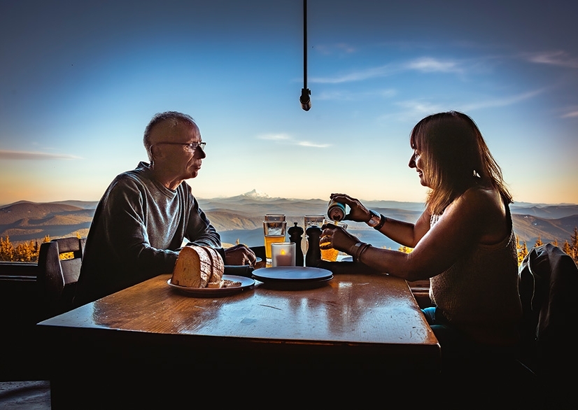 COUPLE ENJOYING THE VIEW OF MT. JEFFERSON FROM A WINDOW SEAT AT TIMBERINE'S RAM'S HEAD BAR, POURING A BEER