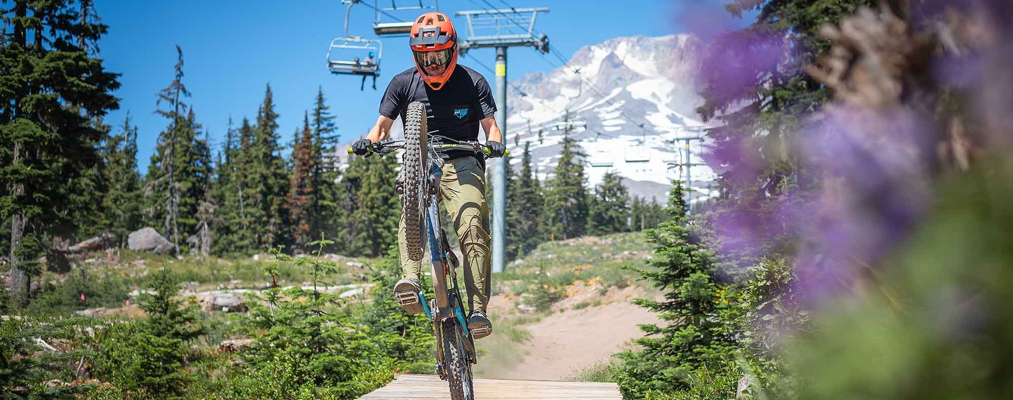 TIMBERLINE BIKE PARK MOUNTAIN BIKER POPPING A WHEELIE ON A BRIDGE WITH MT. HOOD IN THE BACKGROUND