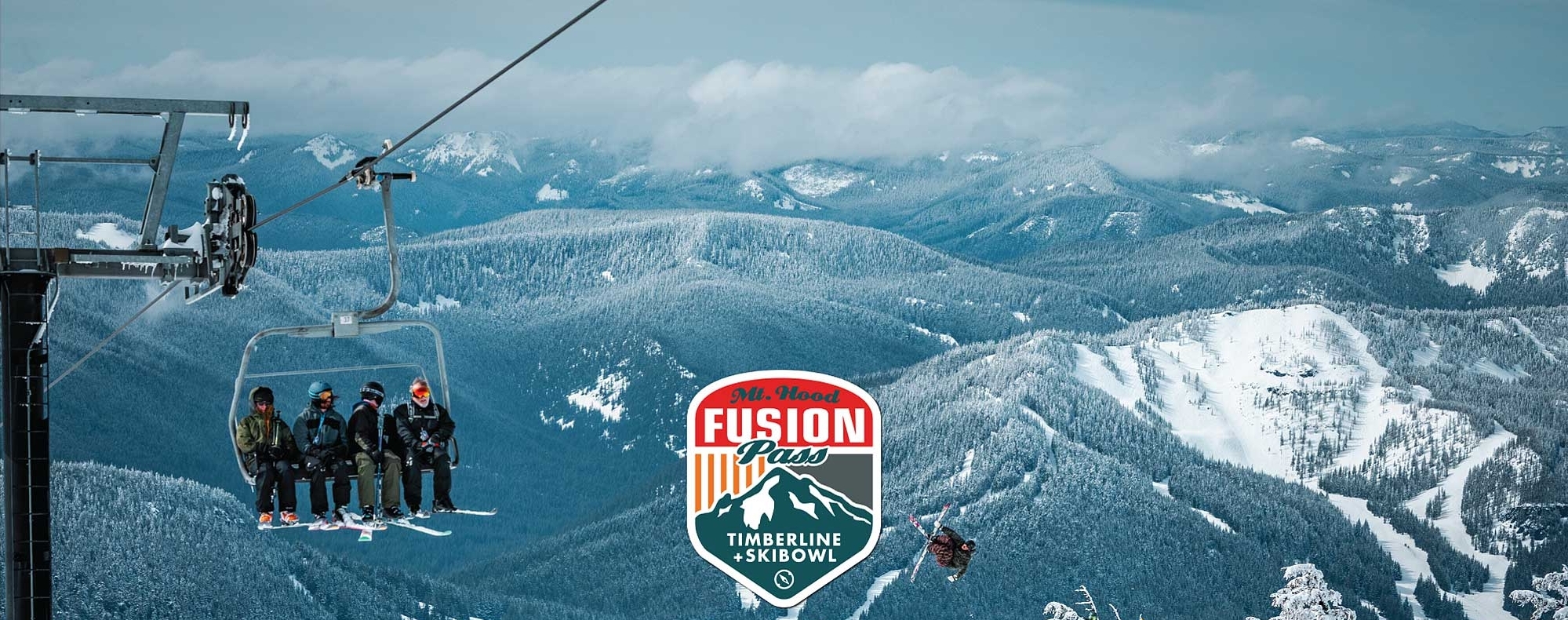 4 SNOWBOARDERS ON A LIFT OVERLOOKING SKIER HITTING A JUMP AT TIMBERLINE WITH SKIBOWL RUNS IN THE BACKGROUND