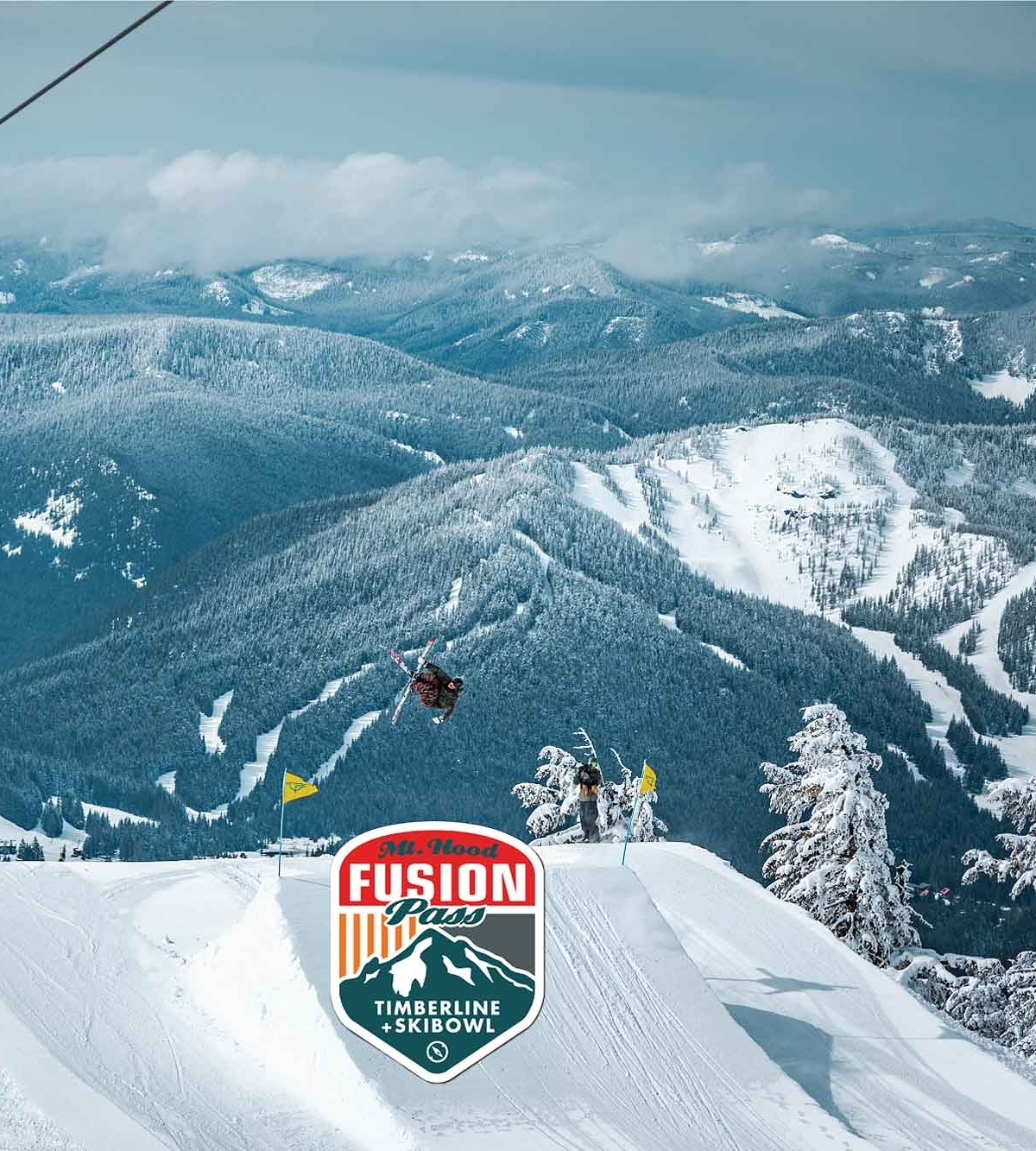 4 SNOWBOARDERS ON A LIFT OVERLOOKING SKIER HITTING A JUMP AT TIMBERLINE WITH SKIBOWL RUNS IN THE BACKGROUND