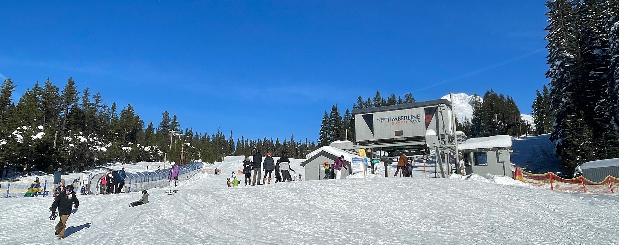 Timberline Summit Pass ski area lower chairlift terminal and covered conveyor, several skiers and snowboarders hanging about