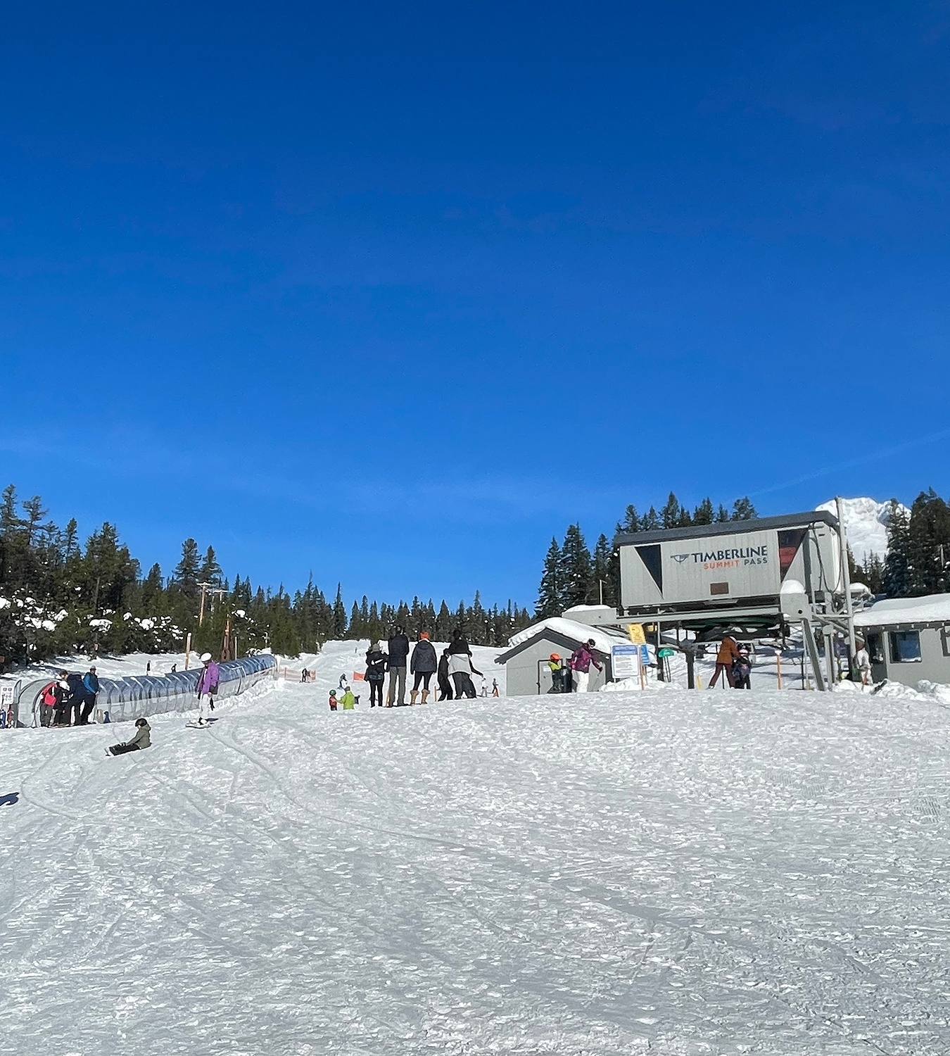 Timberline Summit Pass ski area lower chairlift terminal and covered conveyor, several skiers and snowboarders hanging about