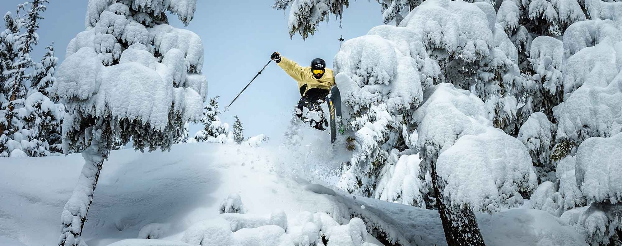 SKIER IN YELLOW JUMPING THROUGH DEEP POW TREES AT TIMBERLINE