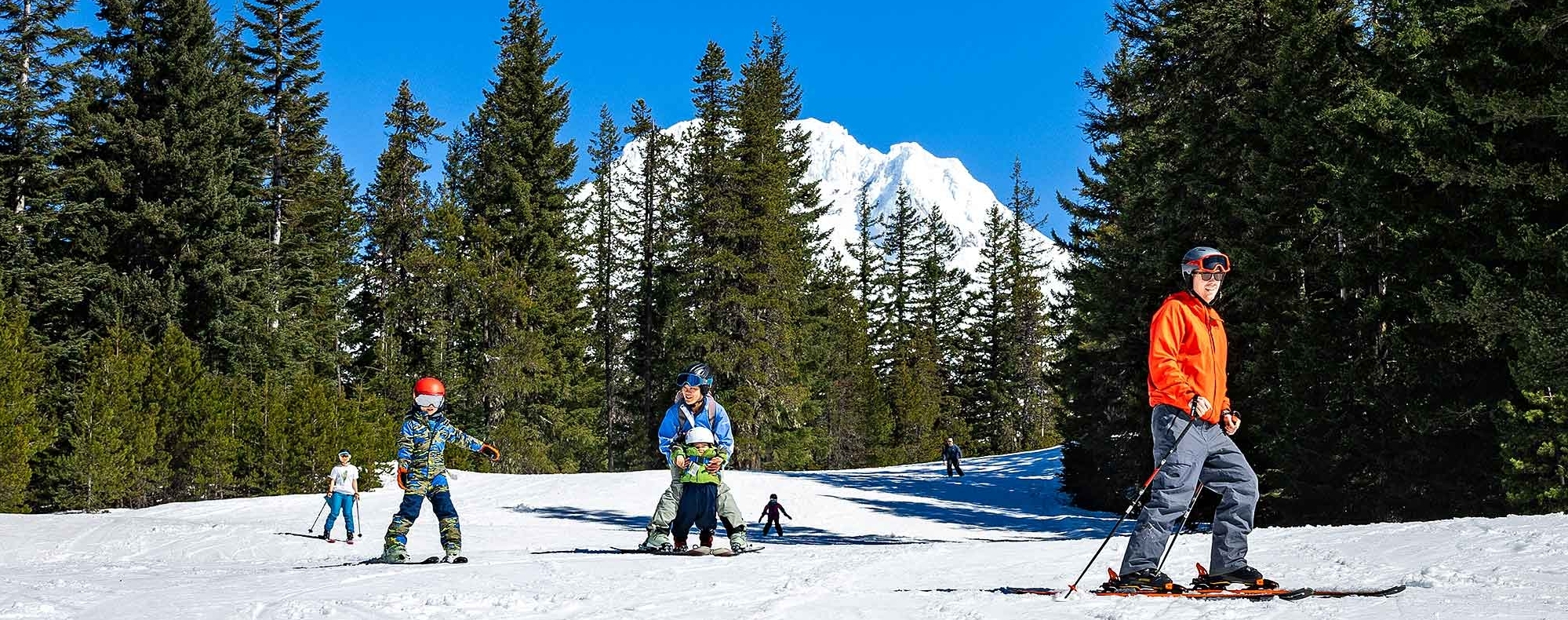 Young family skiing at Timberline Summit Pass on a blue sky day with Mt. Hood in the background