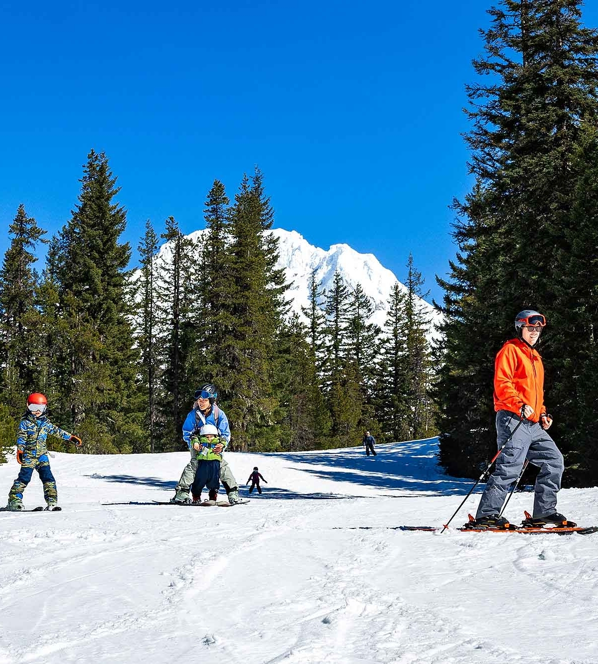 Young family skiing at Timberline Summit Pass on a blue sky day with Mt. Hood in the background