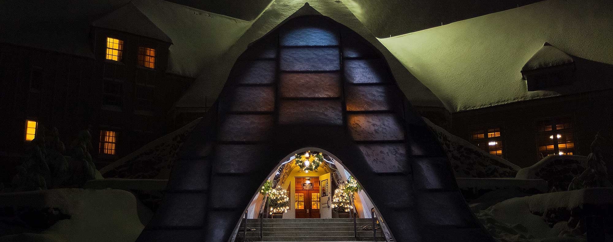 Timberline snow tunnel entrance decorated with garland and lights for the holidays, pictured on a dark and snowy night