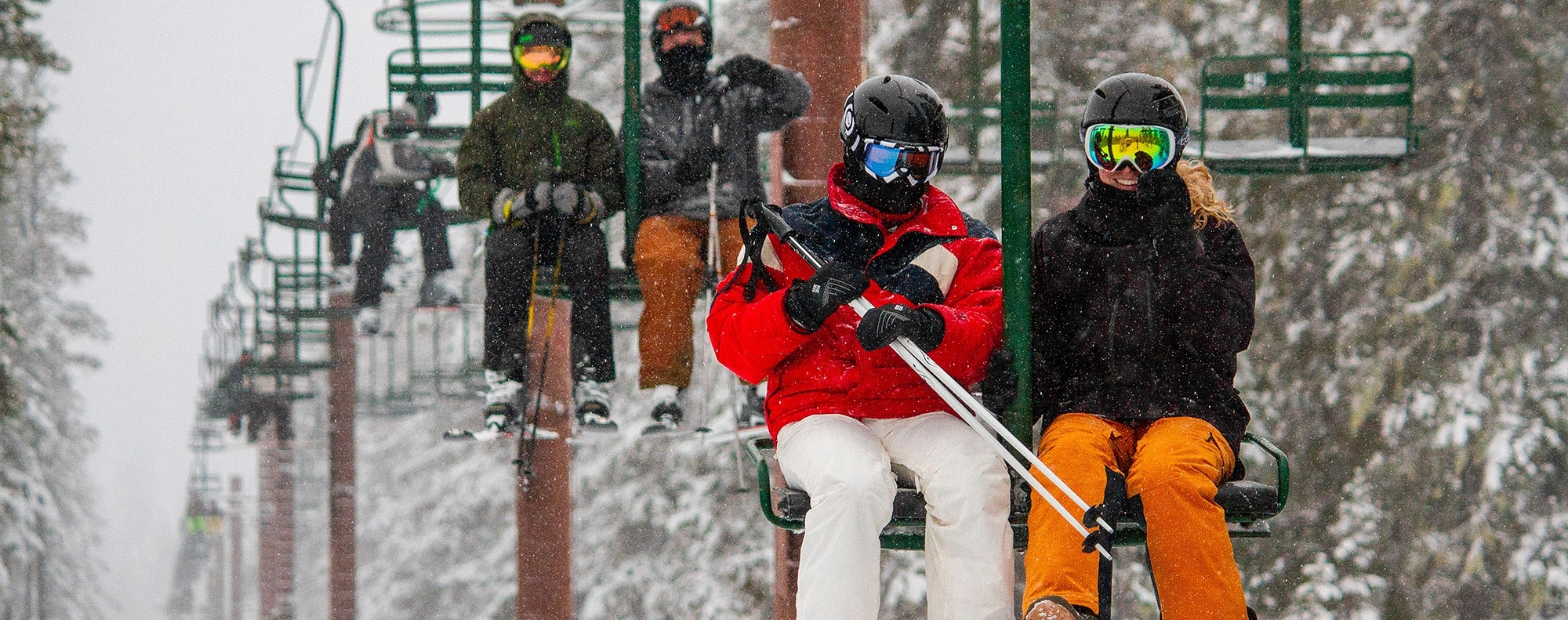 SKIERS RIDING A 2-PERSON CHAIRLIFT IN THE SNOW AT SUMMIT PASS