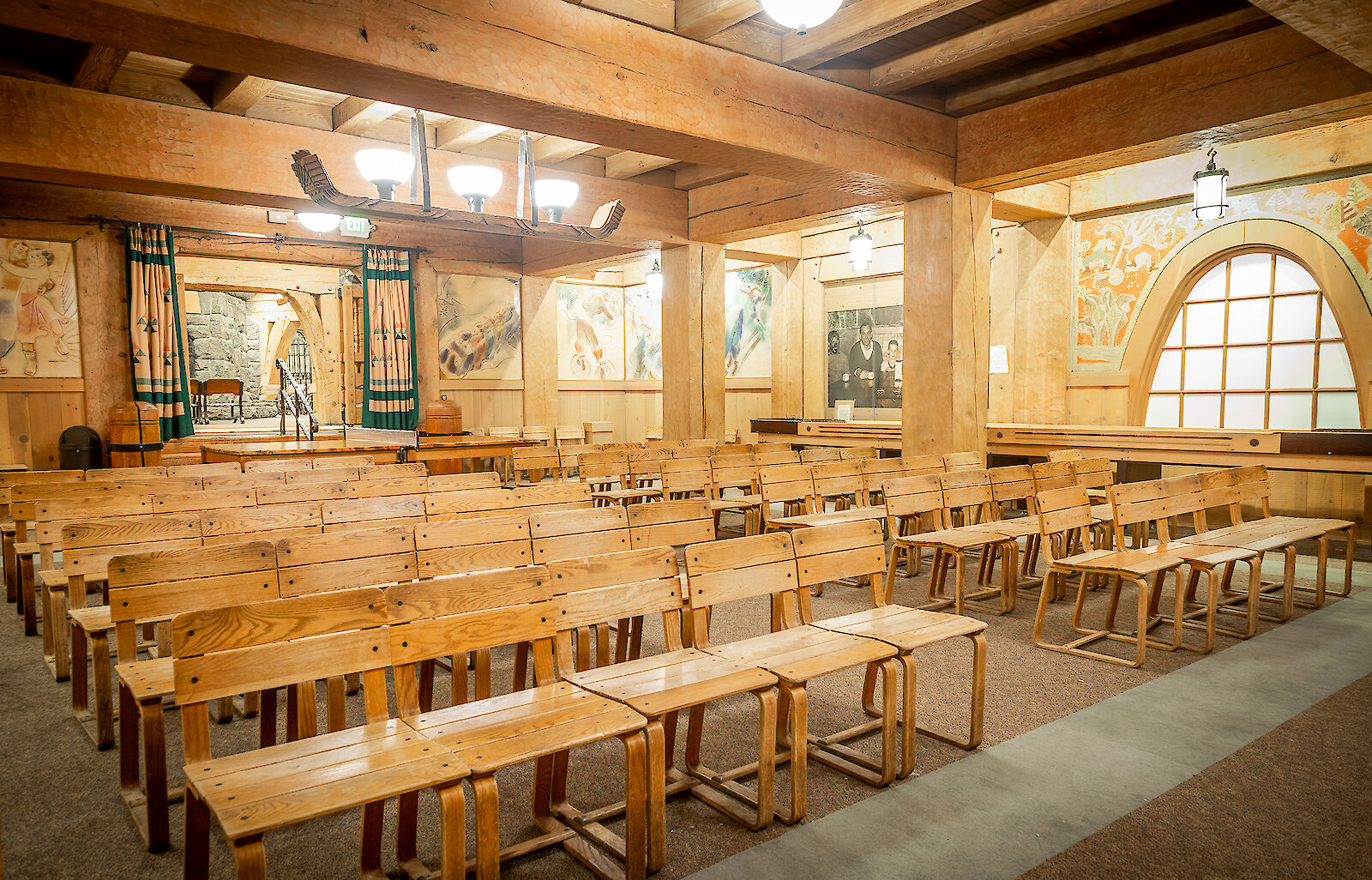 Barlow Room at historic Timberline Lodge on Mt. Hood, featuring handcrafted wooden benches, exposed timber beams, colorful murals, and rustic chandeliers.