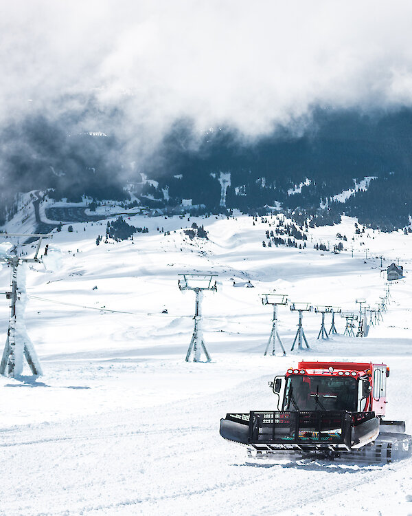 Snowcat grooming a ski slope at Timberline Lodge with snowy lifts and mountain views beneath low-hanging clouds.