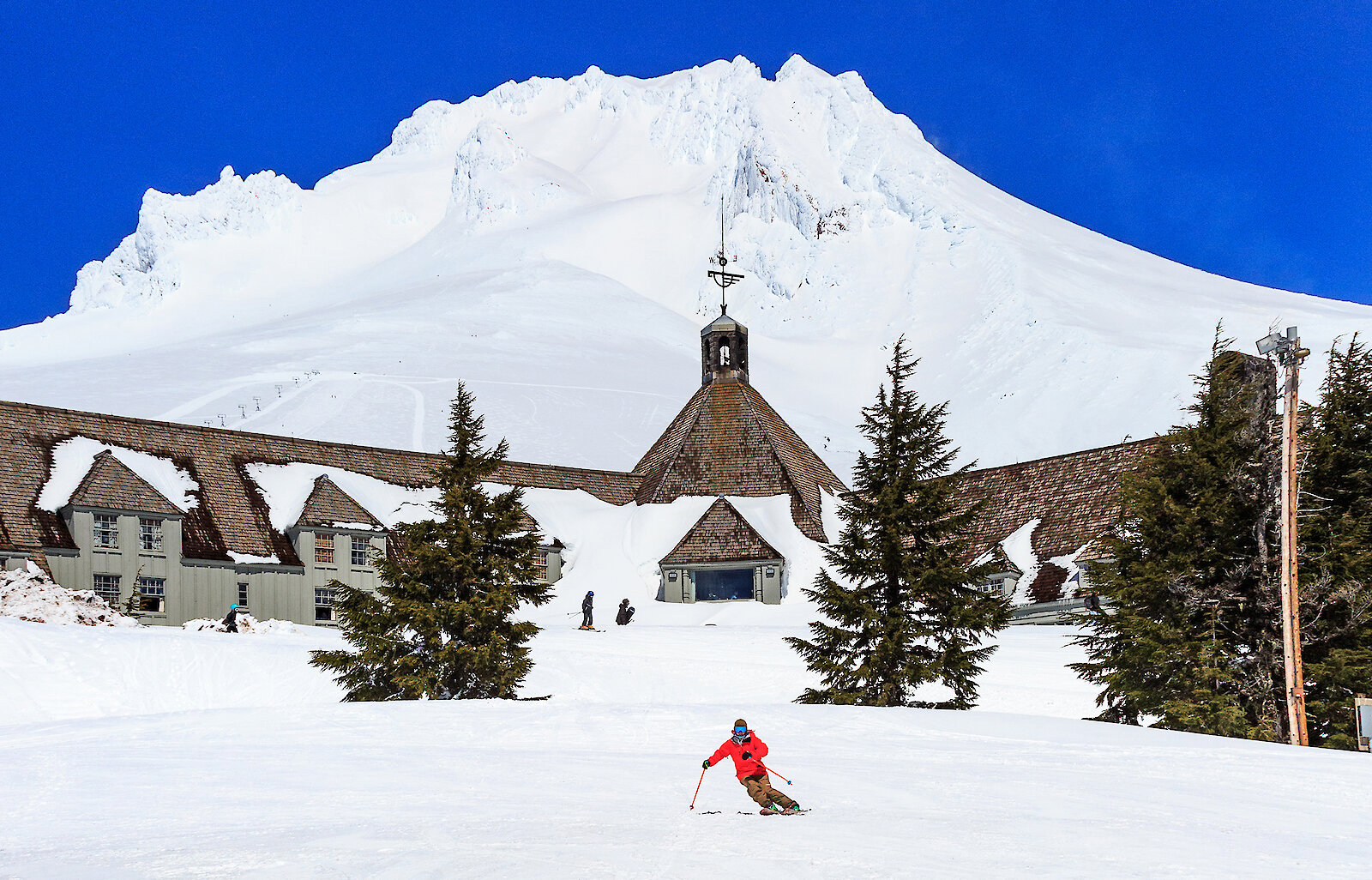 Skier in red jacket skiing in front of Timberline Lodge and Mt. Hood