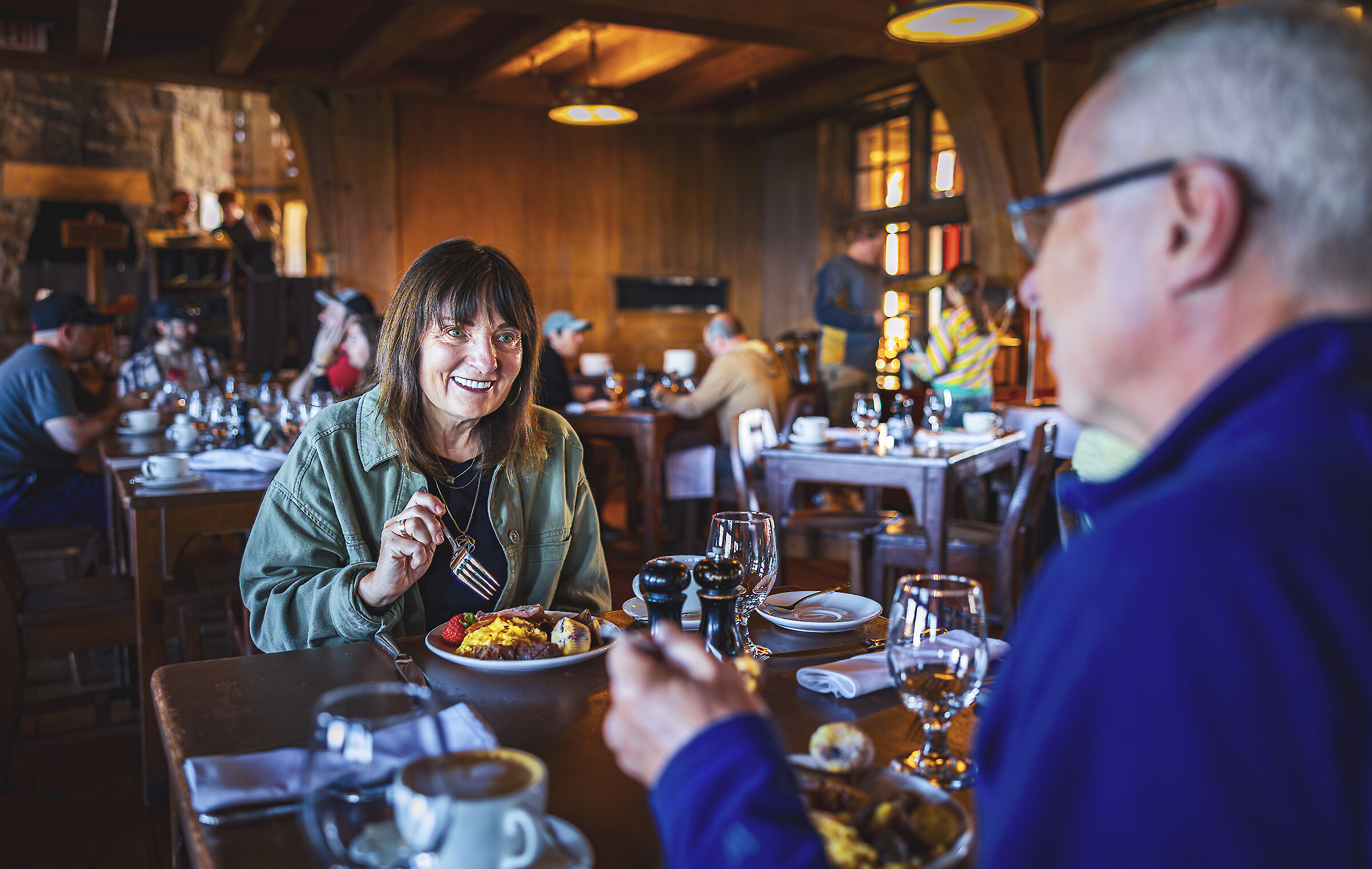 Couple enjoying breakfast at a wooden table inside Timberline Lodge’s dining room, with other guests seated in the background.