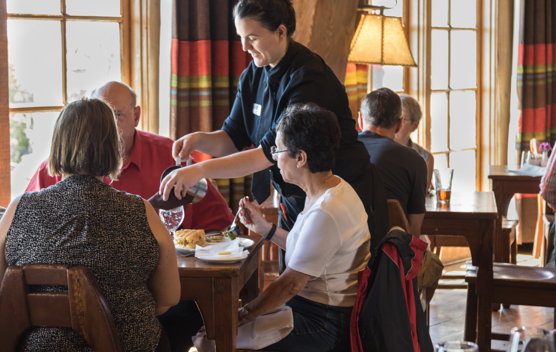 Server pouring coffee for guests seated at a dining table inside Timberline Lodge restaurant with warm wood interiors and natural light.