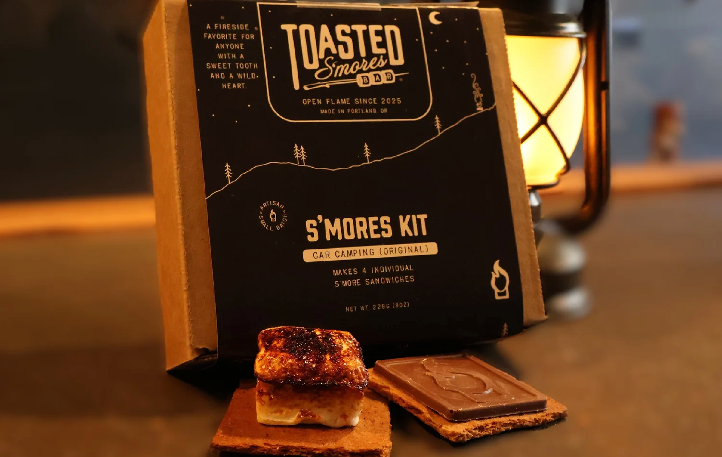 Toasted S’mores Bar car camping s’mores kit with toasted marshmallow, chocolate, and graham cracker displayed in front of branded packaging.