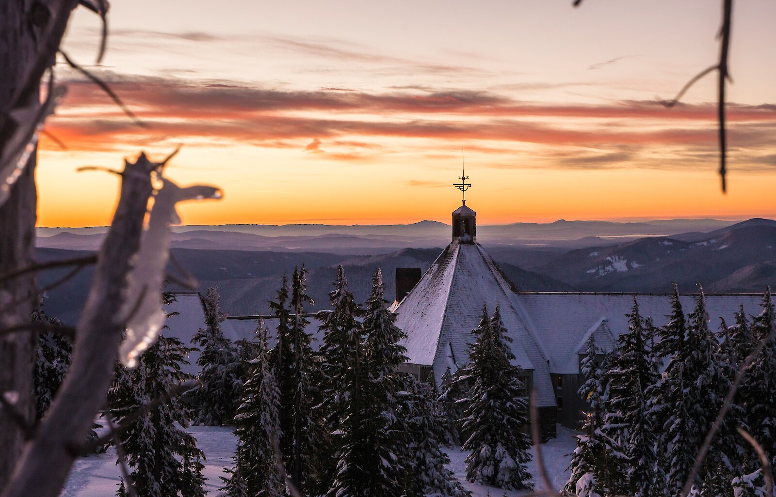 Sunrise view of snow-covered Timberline Lodge with frosted trees and layered mountain horizons
