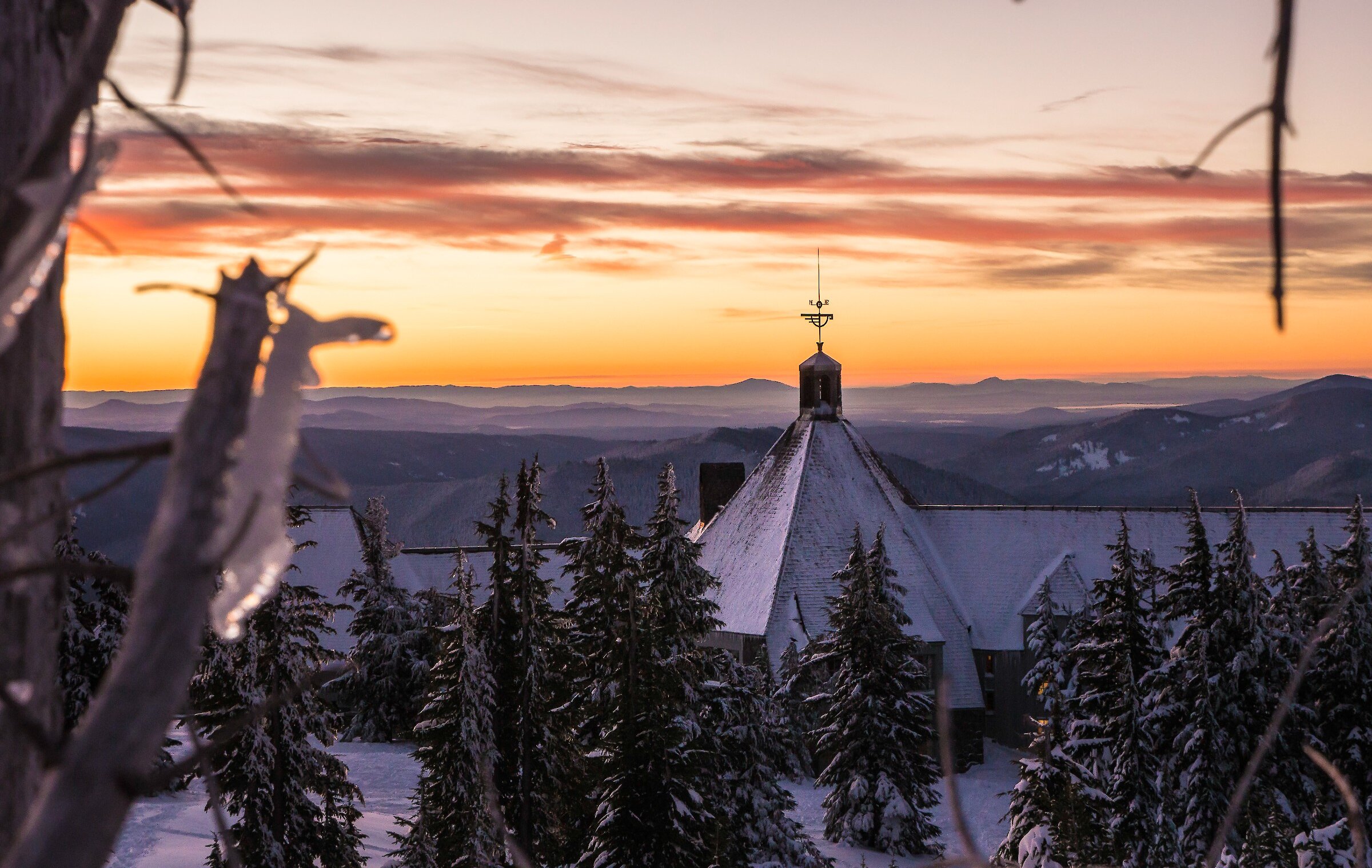 Sunrise view of snow-covered Timberline Lodge with frosted trees and layered mountain horizons