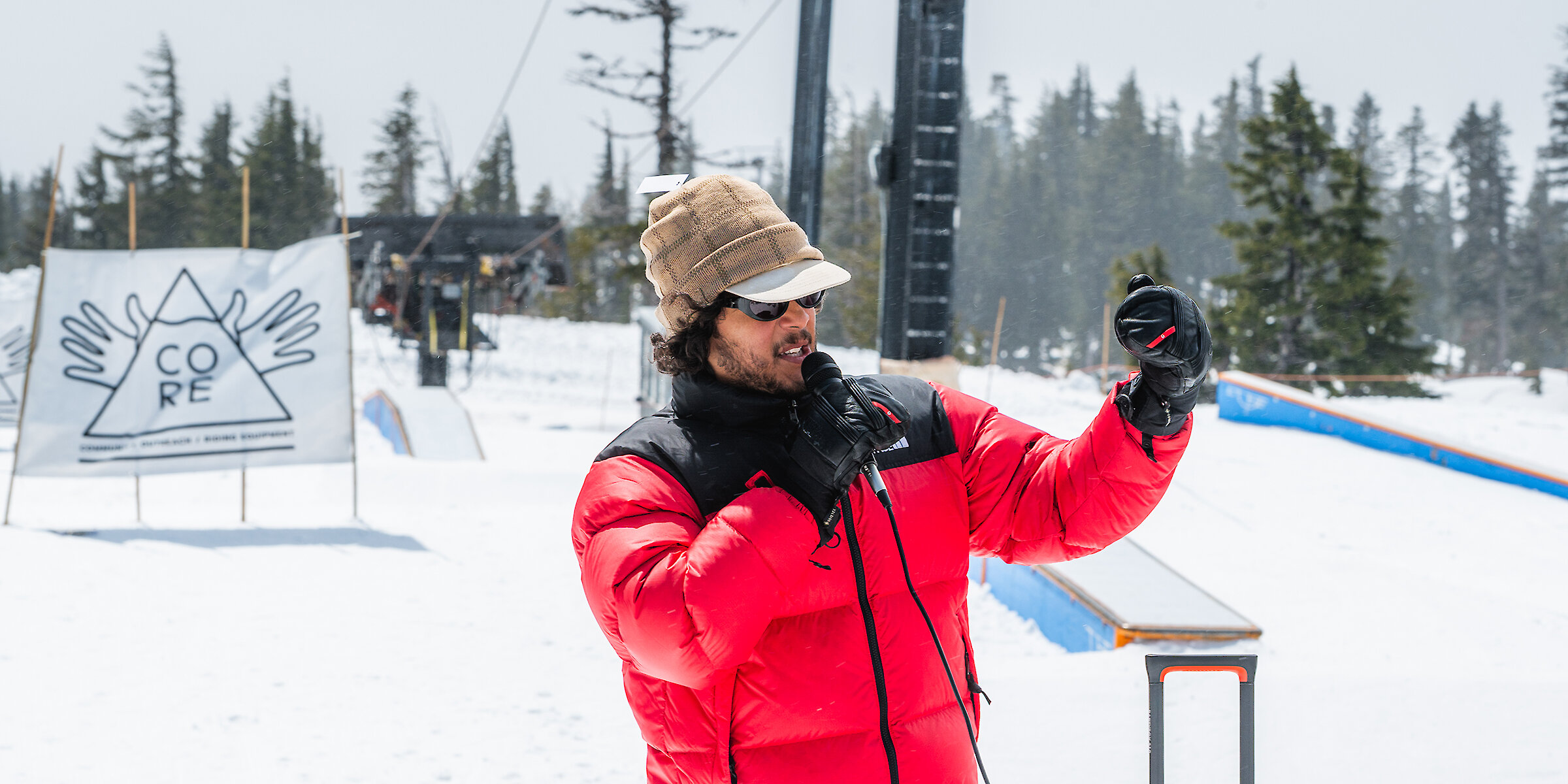Snowboard Erik Leon of CoreNation speaking on a mic at Timberline in front of a Core Snowboarding sign.
