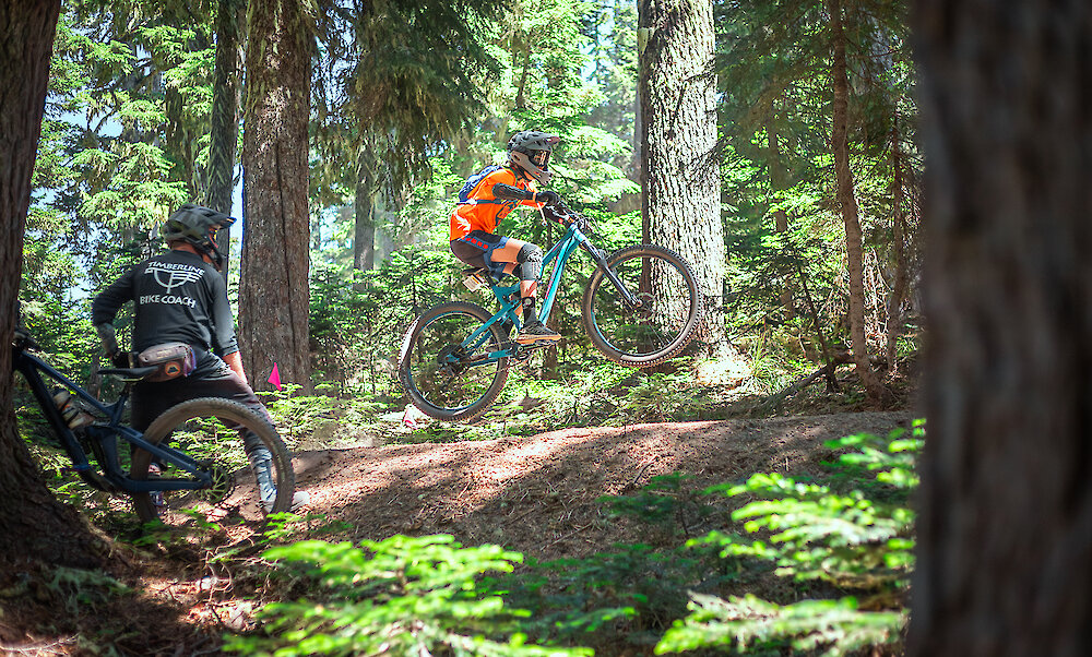 Teen jumping a mountain bike at Timberline while an instructor watches.