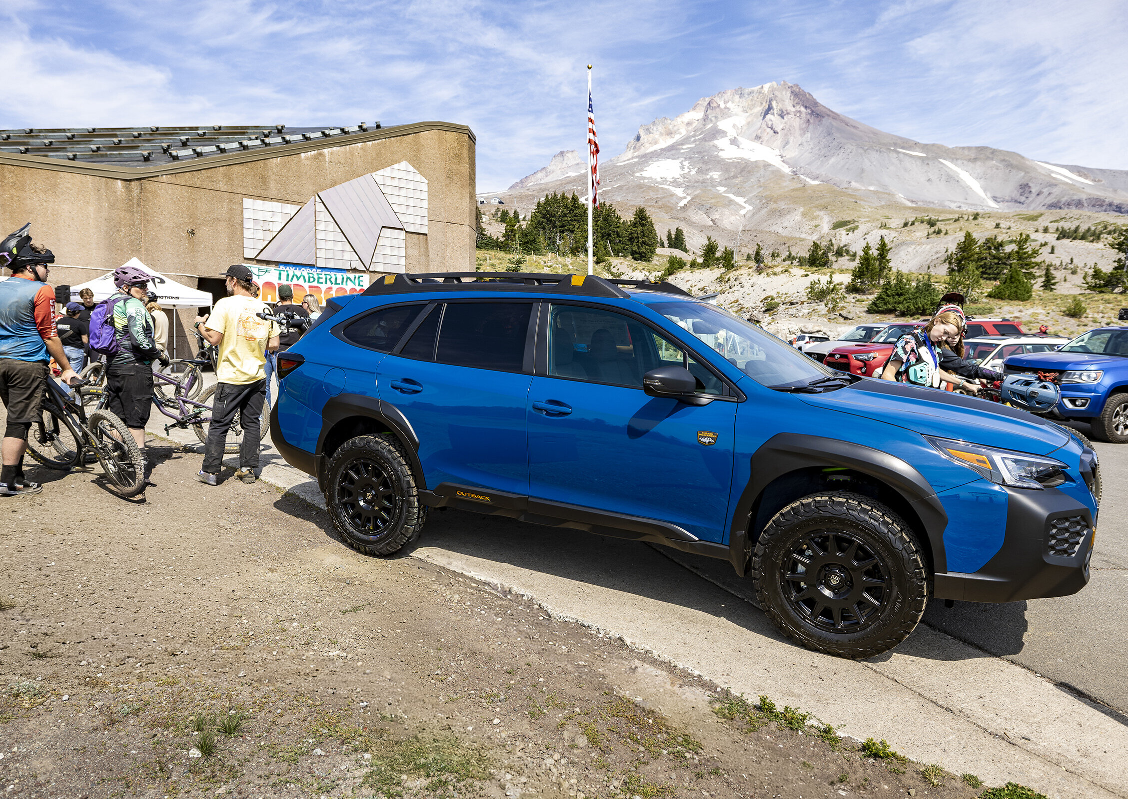 Blue Subaru parked at Timberline with Mount Hood in the background as cyclists gather for the Daydream event on a sunny day.
