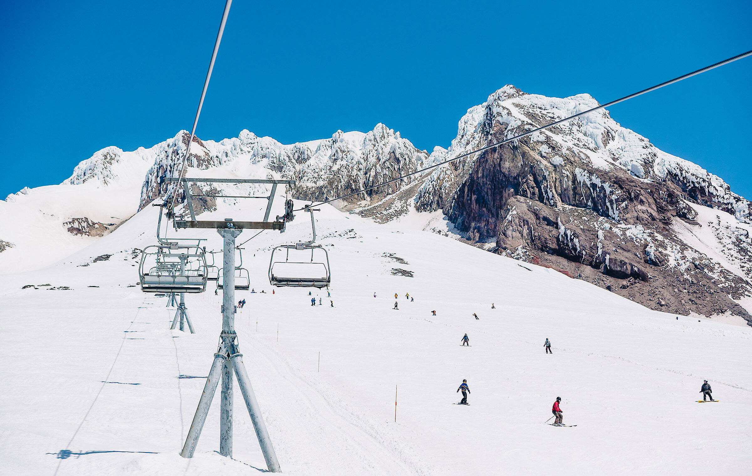 Skiers and snowboarders riding Palmer Snowfield and a blue bird spring day at Timberline