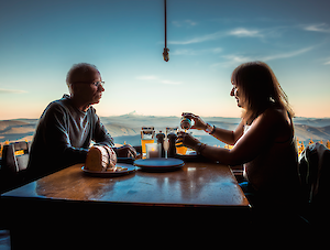 Couple enjoying beers together at the Ram's Head Bar at Timberline, at a table with an incredible view of the sunset over Mt. Jefferson