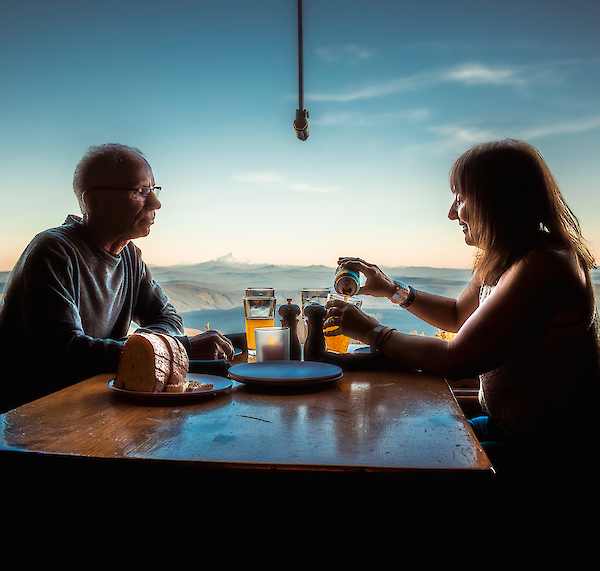 Couple enjoying beers together at the Ram's Head Bar at Timberline, at a table with an incredible view of the sunset over Mt. Jefferson
