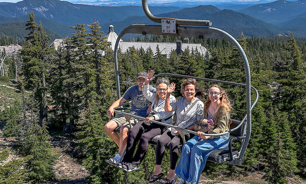 Family of four waving from the Magic Mile Sky Ride with Timberline Lodge in the background