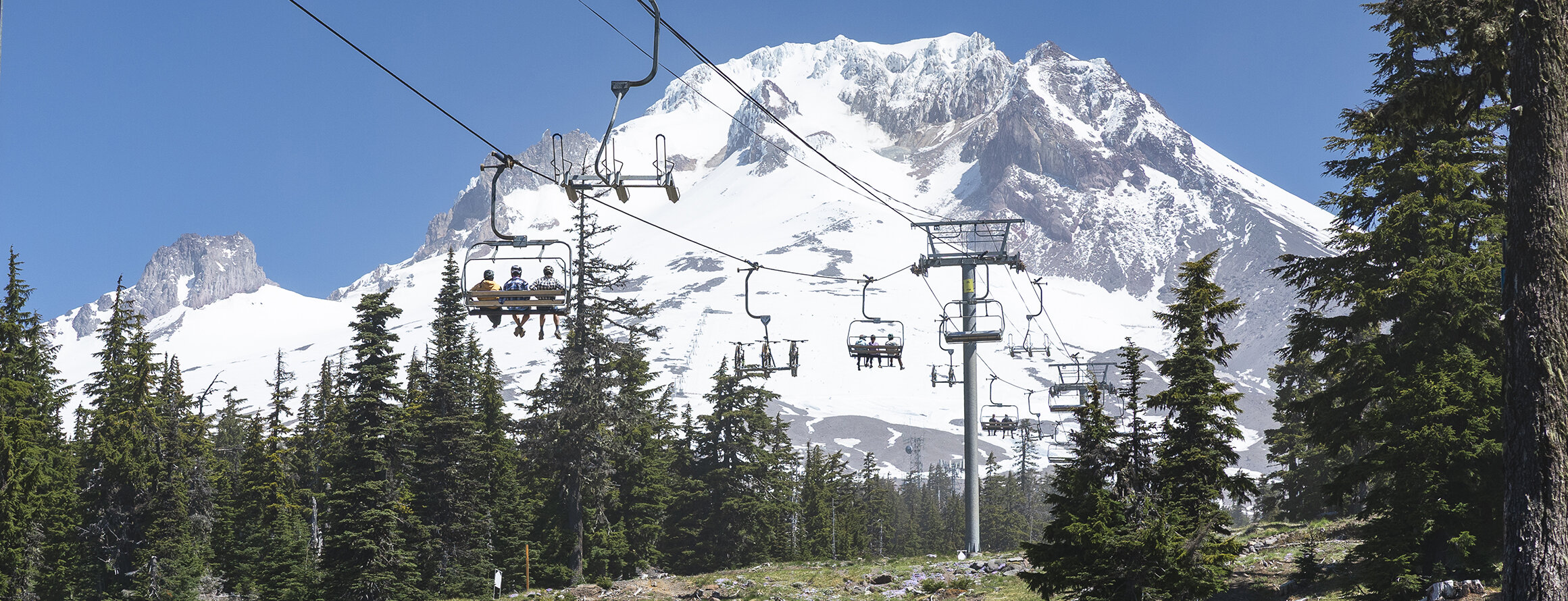 Mountain bikers riding the Jeff Flood lift at the Timberline Bike Park with Mt. Hood in the background