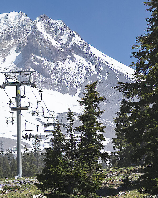 Mountain bikers riding the Jeff Flood lift at the Timberline Bike Park with Mt. Hood in the background