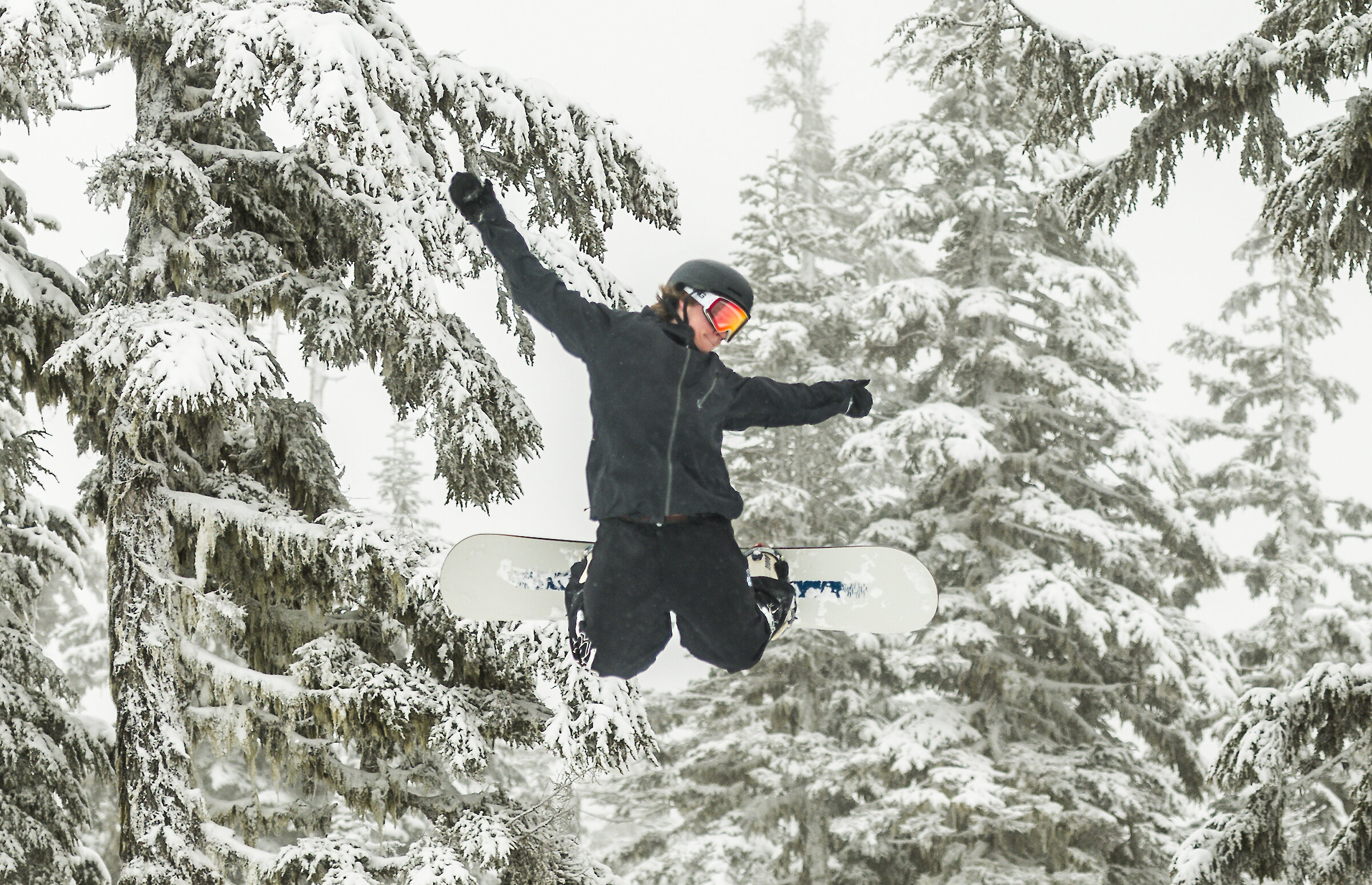 Snowboarder jumping into a tail kick in the snow at Timberline