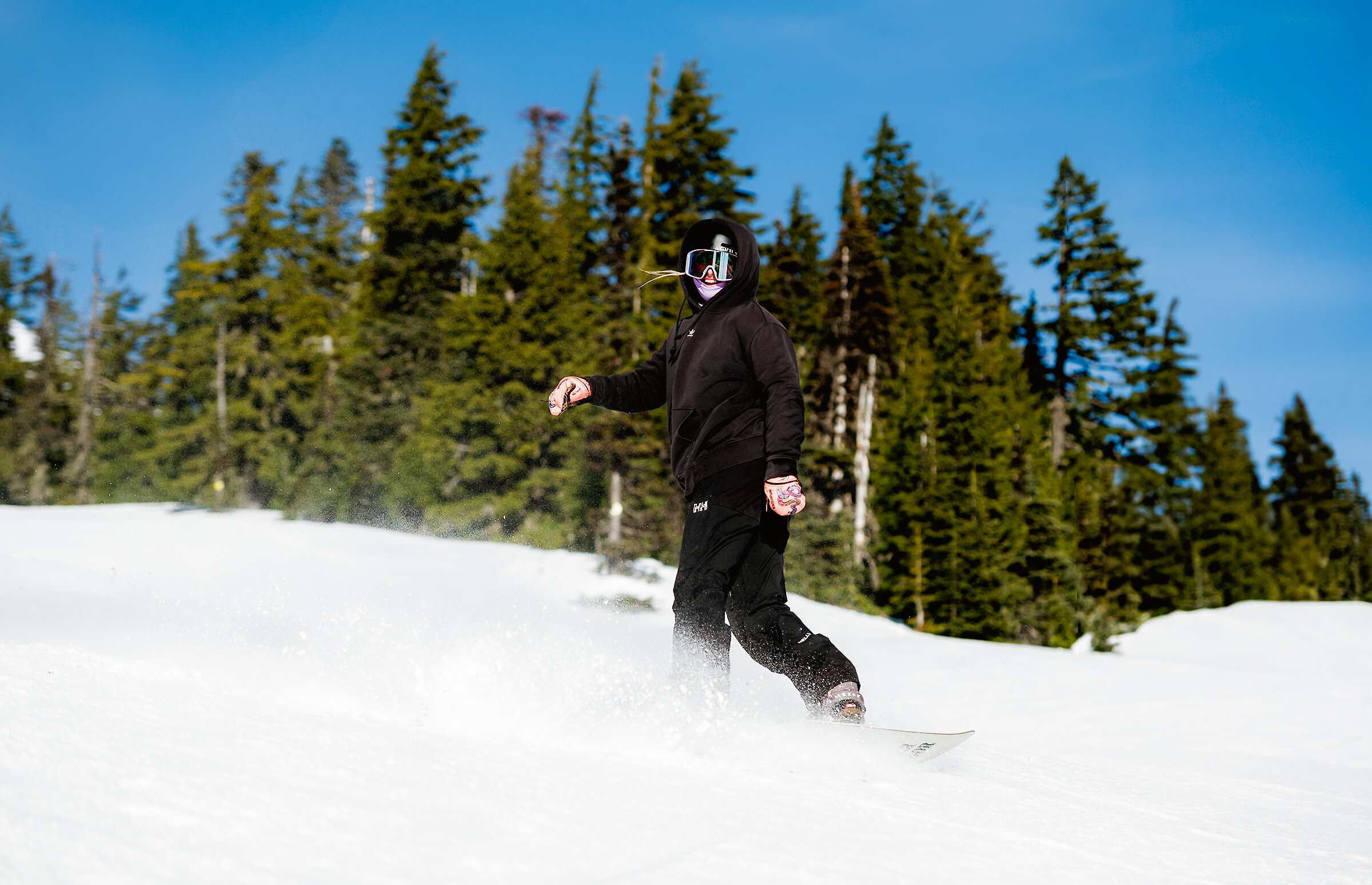Female snowboarder dressed all in black in the snow in front of trees