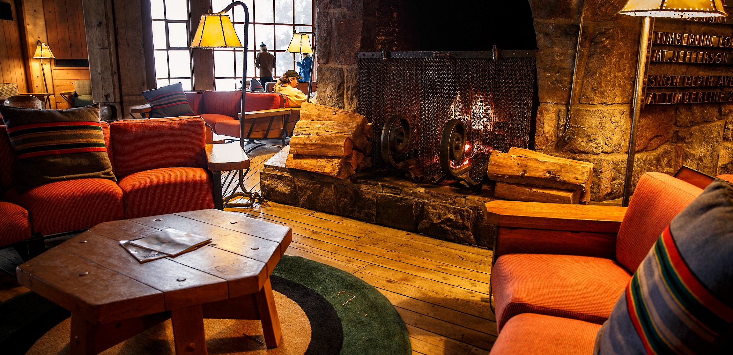 A roaring fire in the massive fireplace, surrounded by couches and a table in the Timberline Main Headhouse
