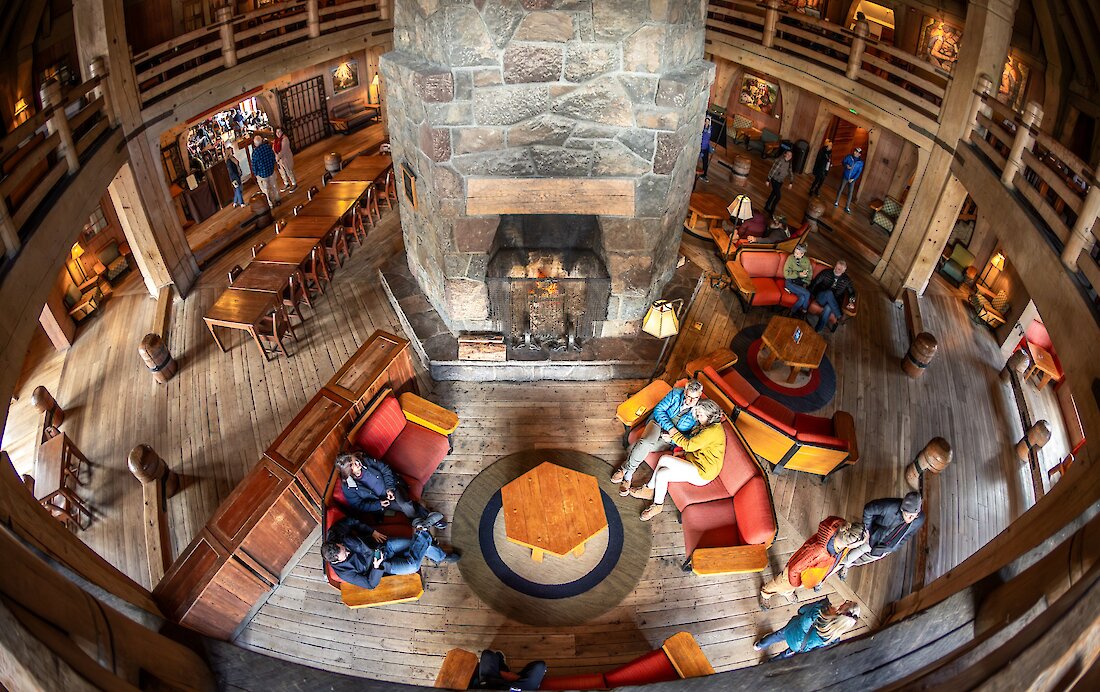 People enjoying the Main Headhouse at Timberline Lodge, sitting in couches around the massive fireplace.