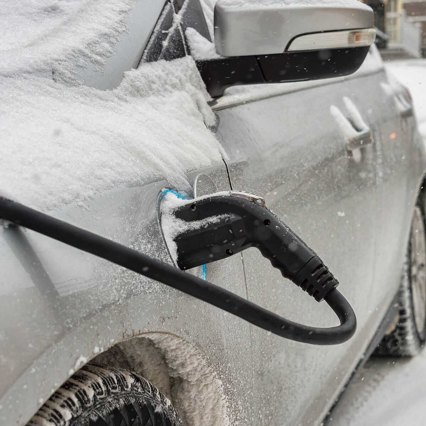 Snow-covered car with an EV charging cable plugged into it