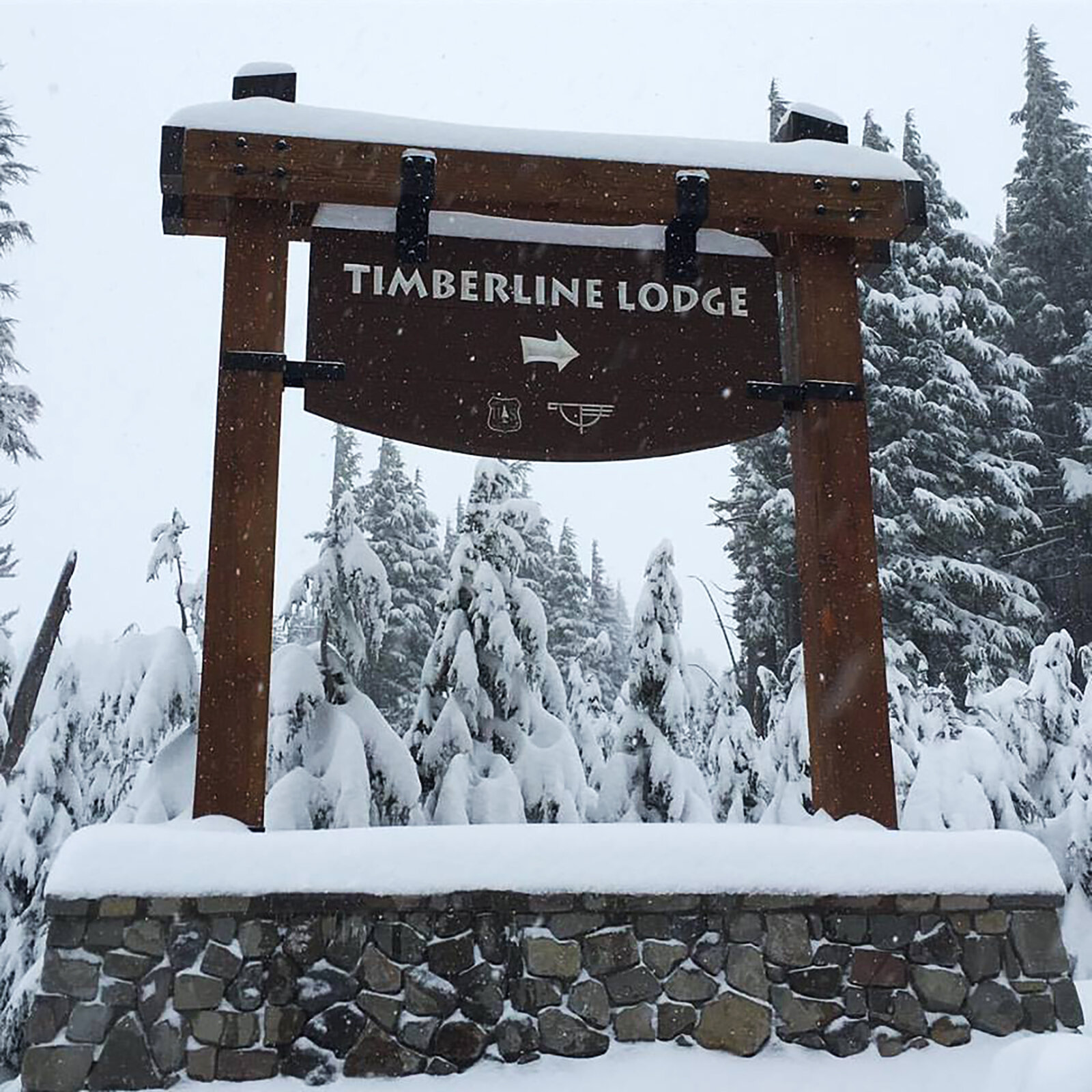 Timber-framed sign for Timberline Lodge with arrow pointing right covered in snow