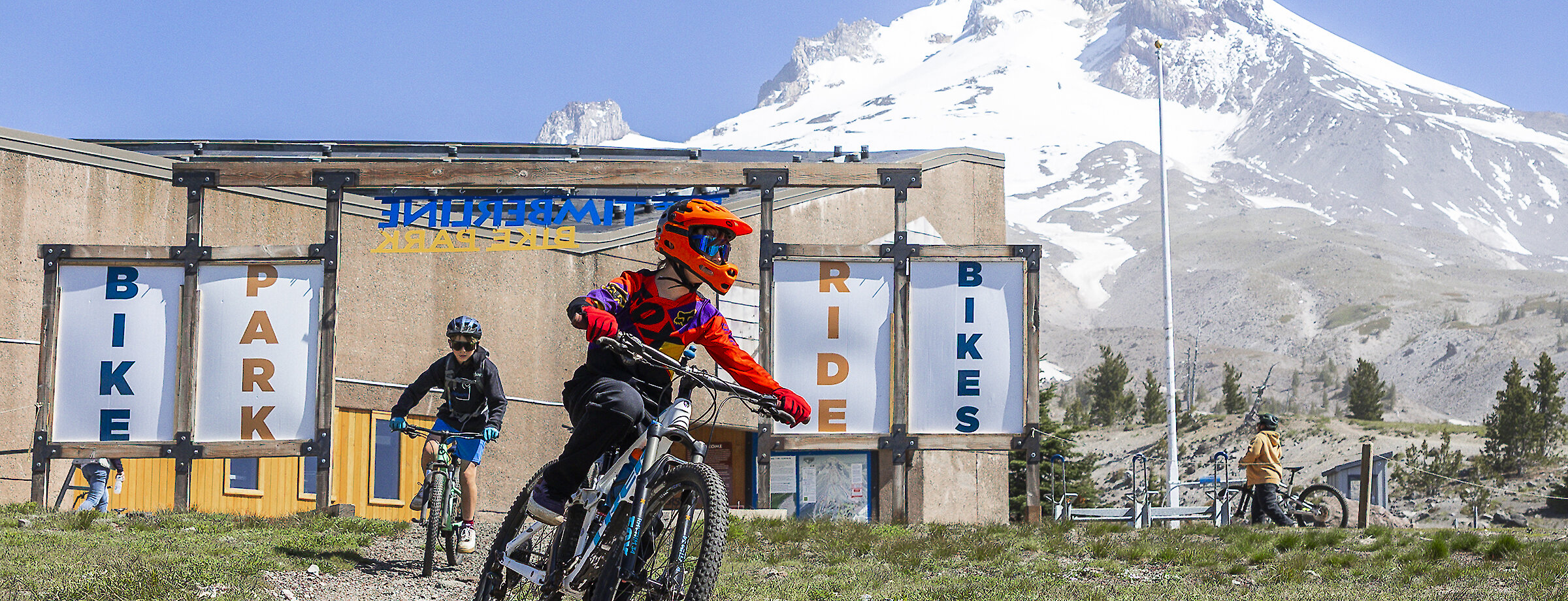 Two mountain bikers entering the Timberline Bike Park with a view of Mt. Hood behind them.
