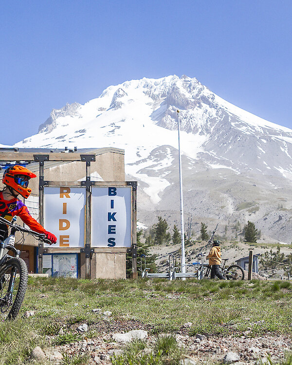 Two mountain bikers entering the Timberline Bike Park with a view of Mt. Hood behind them.