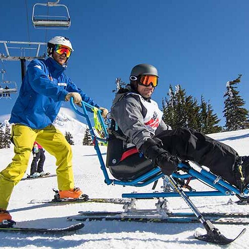 Adaptive skier in a sit-ski with an assist by a skier on Mt. Hood