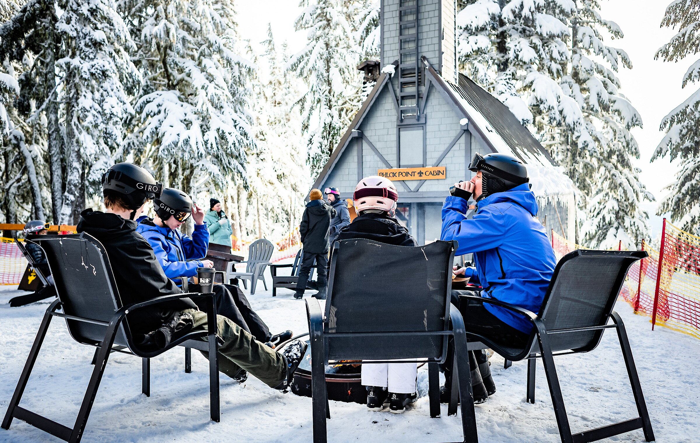 Skiers and snowboarders munching on tacos and enjoying drinks gathered around the fire outside at Phlox Point Cabin