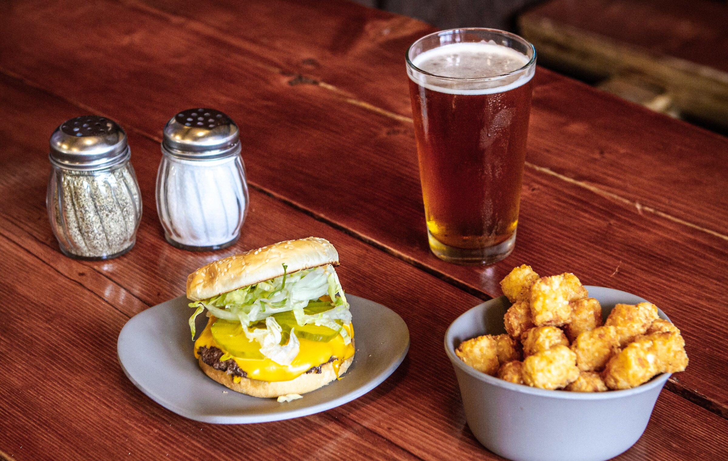 A burger, tater tots, pint of beer, and salt & pepper shaker pictured on a wood table at Summit Pass Cafe