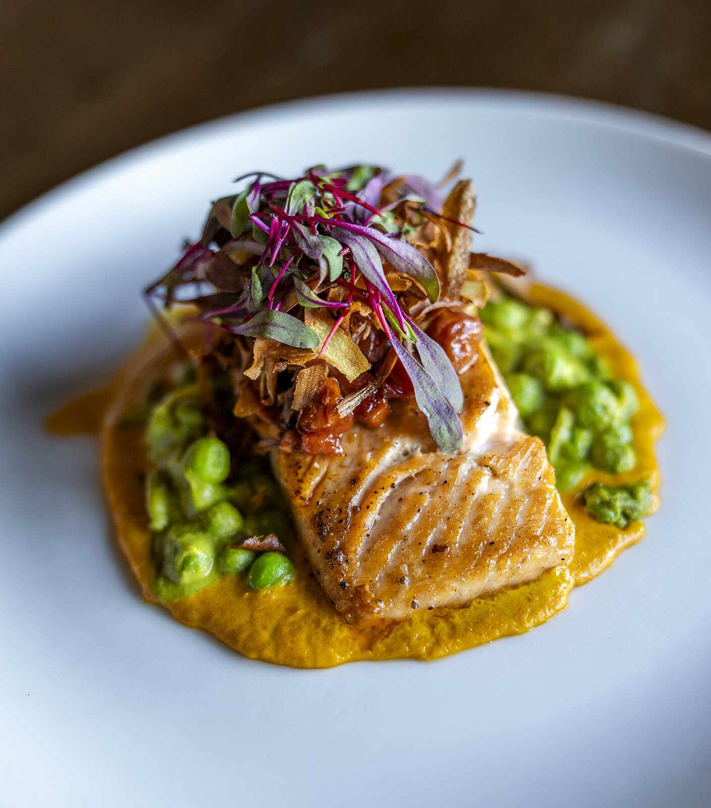 Roasted salmon with creamy english peas, sweet corn puree, cherry bacon jam, fried parsnips, served up on a white plate in the Cascade Dining Room