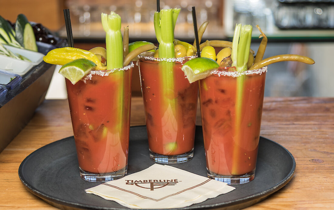 Three Bloody Marys with garnishes on a tray with a Timberline logo cocktail napkin in the Ram's Head Bar