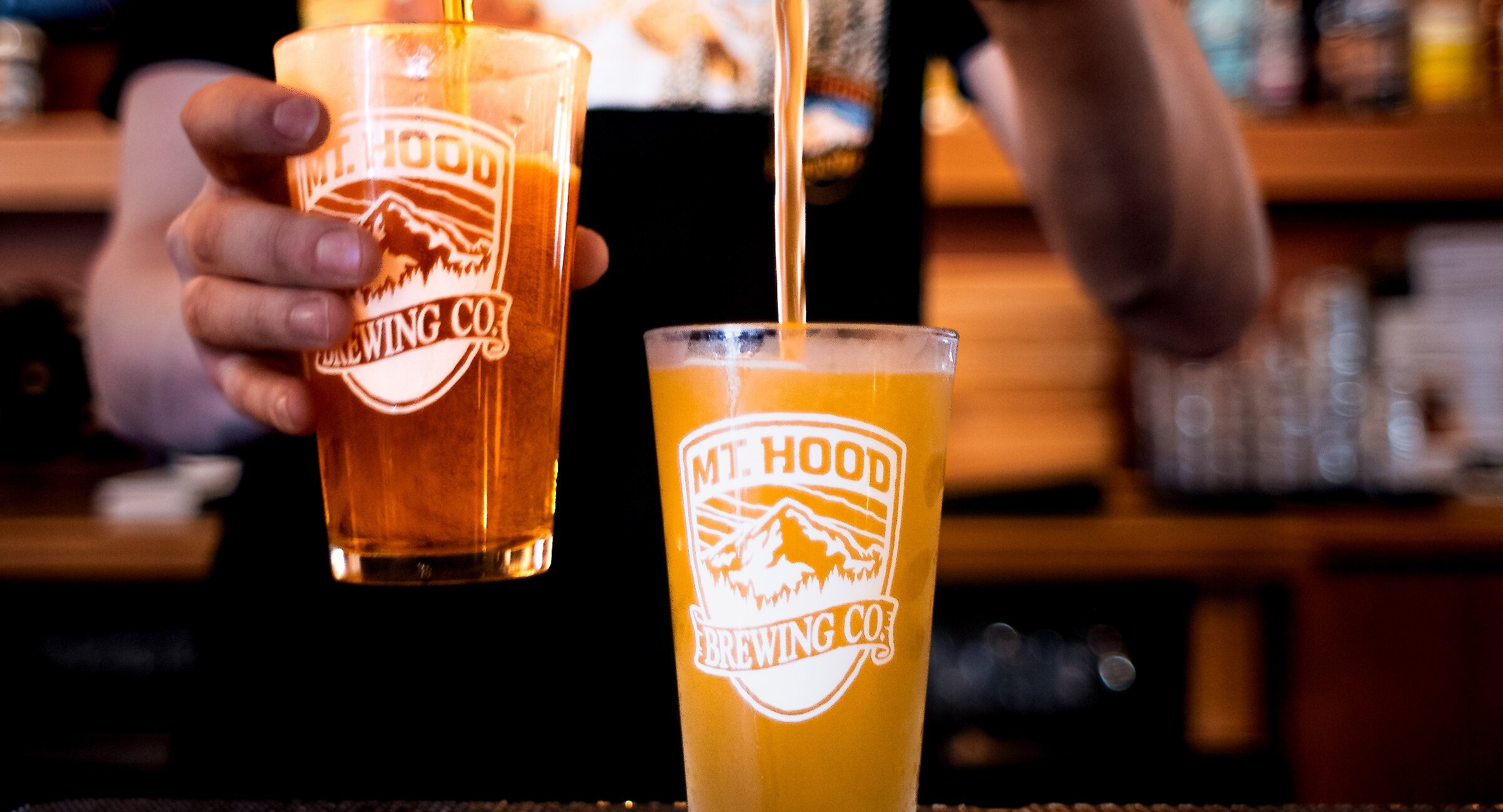 Bartender pouring two pints of Mt. Hood Brewing Co. craft ales into logoed glasses
