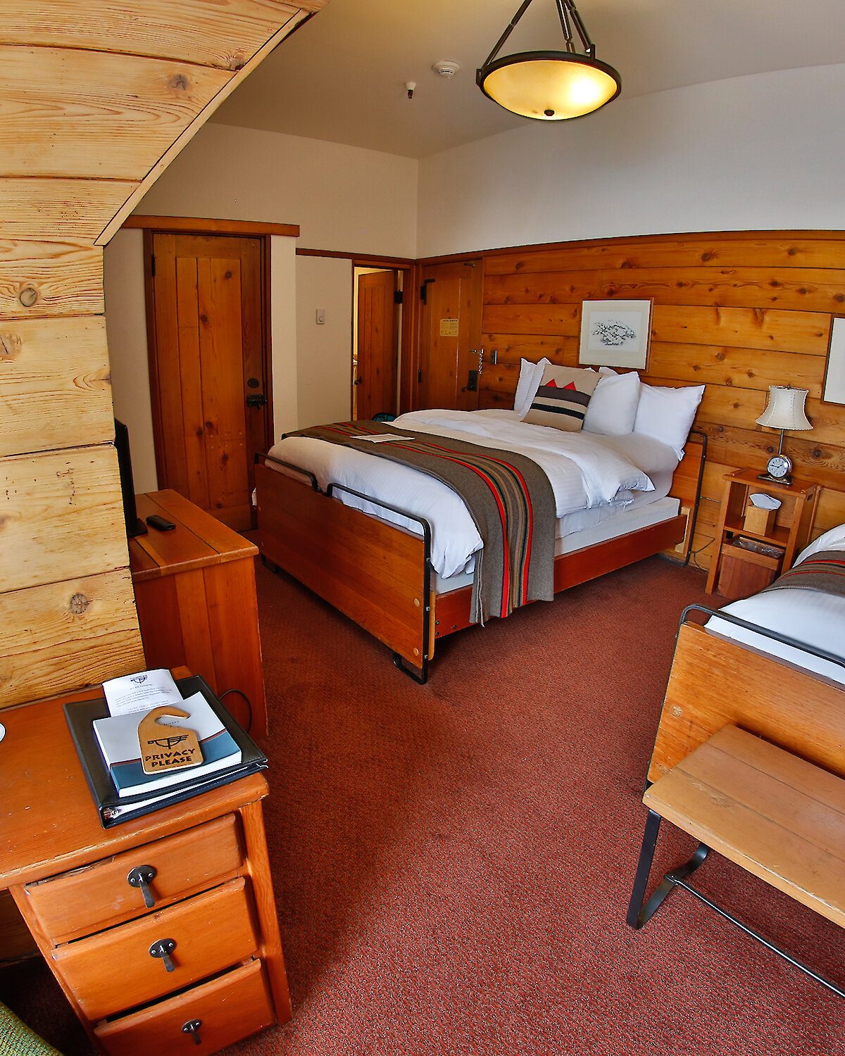 A Timberline queen + twin room pictured with a Pendleton blankets draped over the beds, a small desk and mirror, and wood-paneled walls.