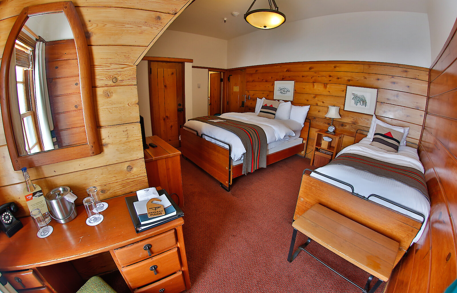 A Timberline queen + twin room pictured with a Pendleton blankets draped over the beds, a small desk and mirror, and wood-paneled walls.