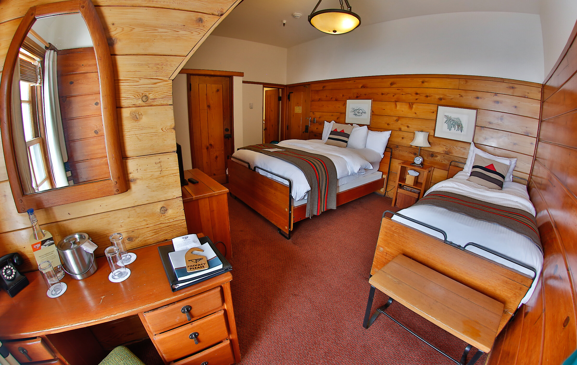 A Timberline queen + twin room pictured with a Pendleton blankets draped over the beds, a small desk and mirror, and wood-paneled walls.