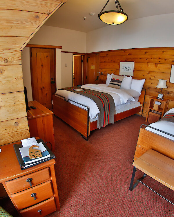 A Timberline queen + twin room pictured with a Pendleton blankets draped over the beds, a small desk and mirror, and wood-paneled walls.