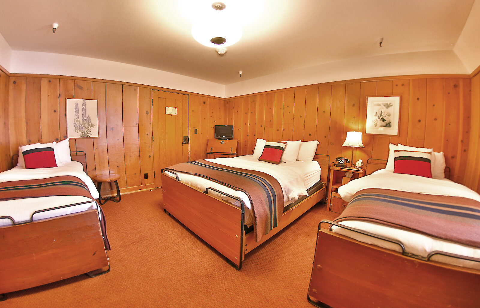 A Timberline queen + two twins room pictured with a Pendleton blankets draped over the beds and wood-paneled walls.