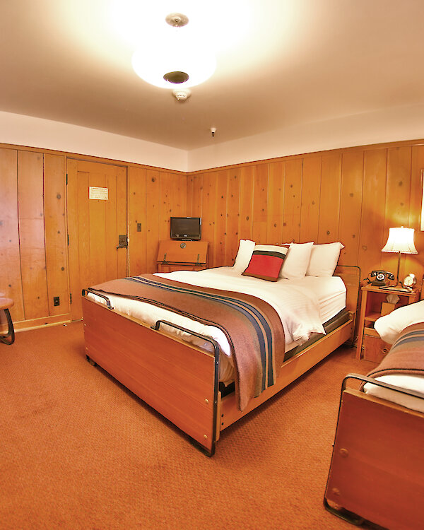 A Timberline queen + two twins room pictured with a Pendleton blankets draped over the beds and wood-paneled walls.